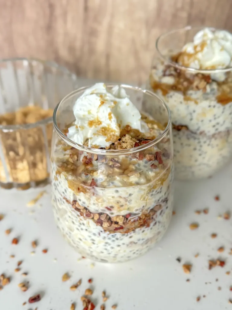 Two servings of maple pecan and brown sugar overnight oats in glasses on a counter next to a bowl of chopped pecans.