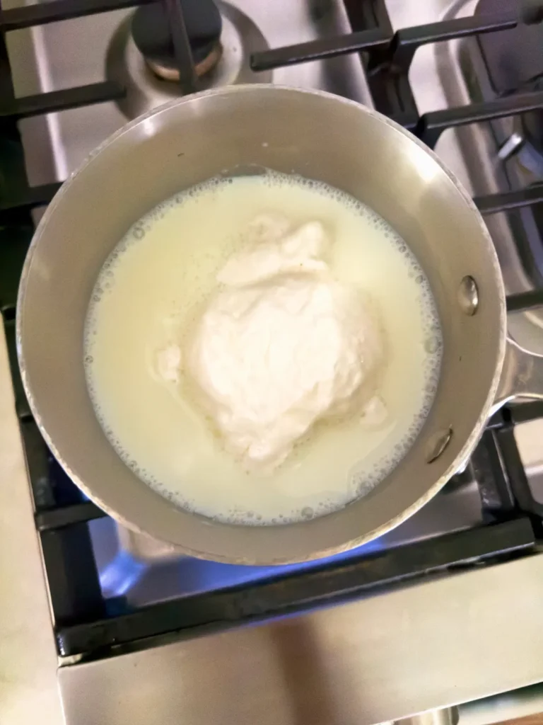 A pot on the stove with milk and marshmallow cream in it. 