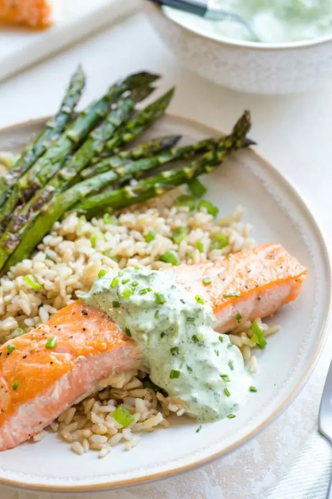 Pan-seared salmon topped with basil tzatziki sauce on a plate next to asparagus.