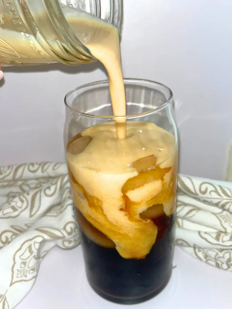 Pouring the pumpkin spice cold foam into a glass of ice coffee.