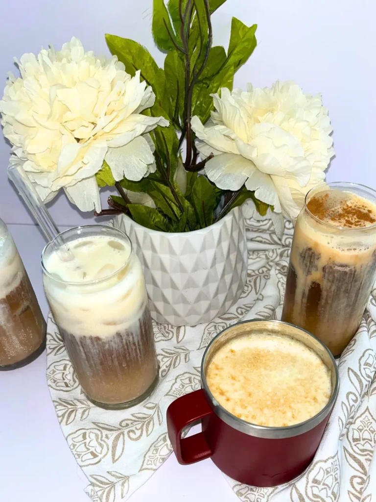 4 protein coffees on a white towel on a counter next to a pot of white flowers.