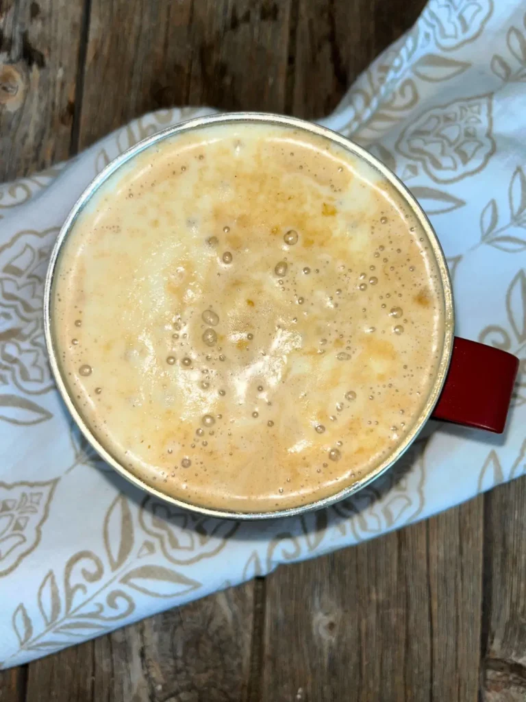 A hot cup of coffee topped with protein cold foam on a wooden cutting board.