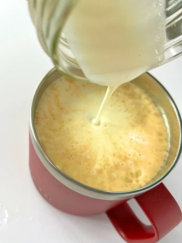 Pouring the cold foam from a mason jar onto a hot cup of coffee.