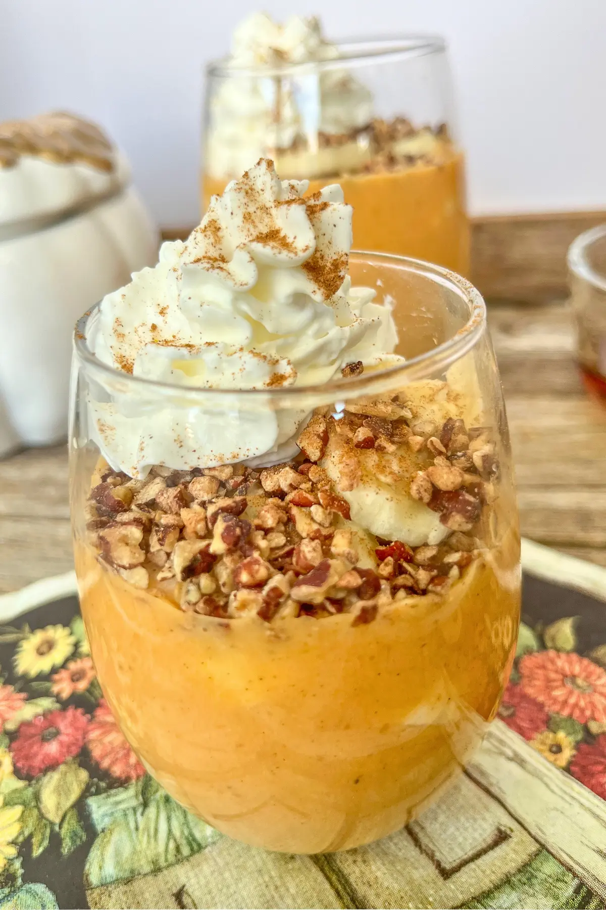 A glass of two pumpkin protein puddings on a counter next to a pumpkin decoration.
