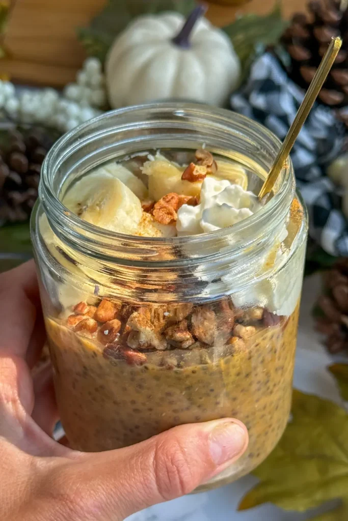 Someone holding a mason jar with protein pudding in it with a golden spoon in it as well. 