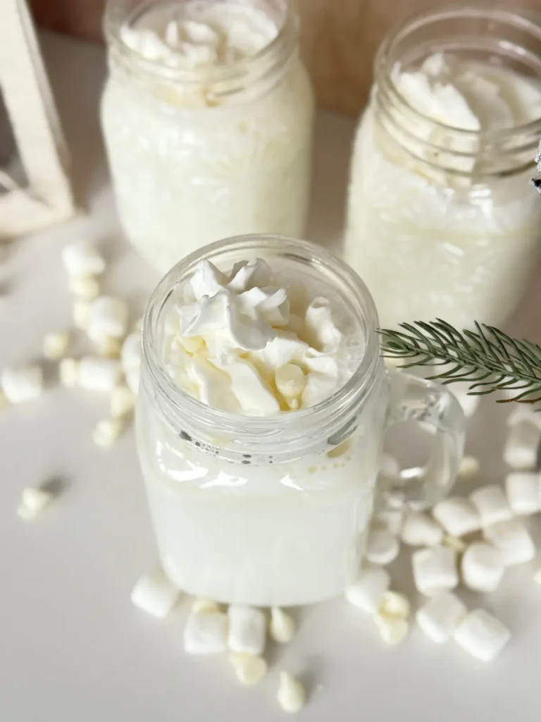 A birds-eye view of three glass mugs filled with white chocolate and marshmallow cream hot cocoa topped with whipped cream on a counter.