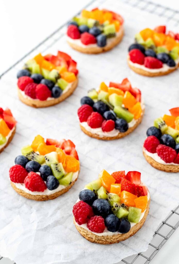 Mini fruit pizzas in the shape of an egg on parchment paper on a cooling rack.