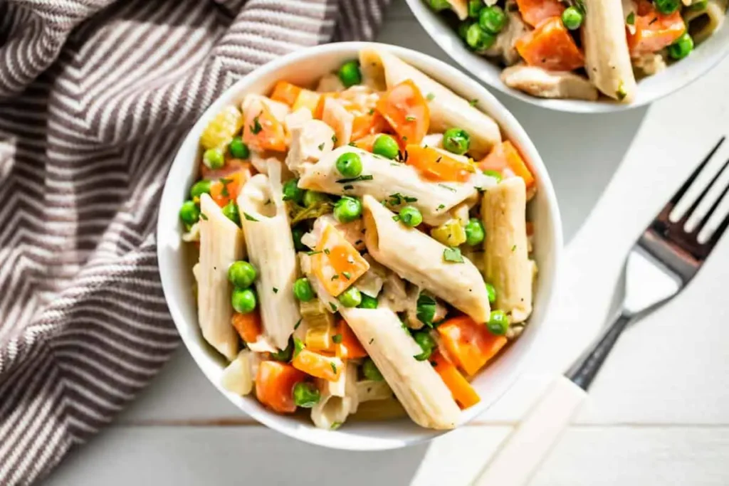 A bowl of chicken pot pie pasta on a table next to a fork and a dish towel.