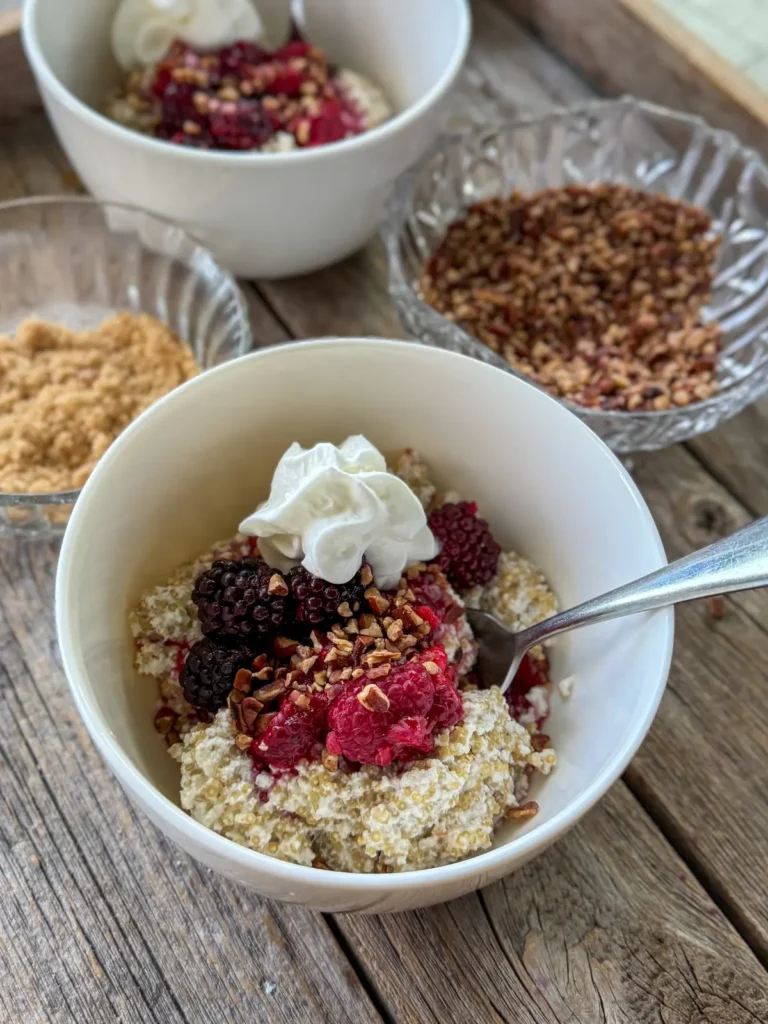 Two bowls of quinoa made with coconut milk topped with frozen berries on a wooden platter.