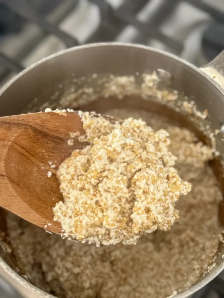 Creamy coconut quinoa on a wooden spoon with the pan in the background.