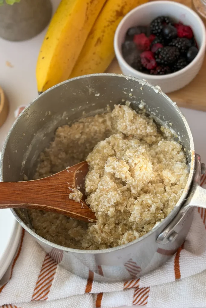 A pot of coconut milk quinoa with a wooden spoon in it on a table next to berries.
