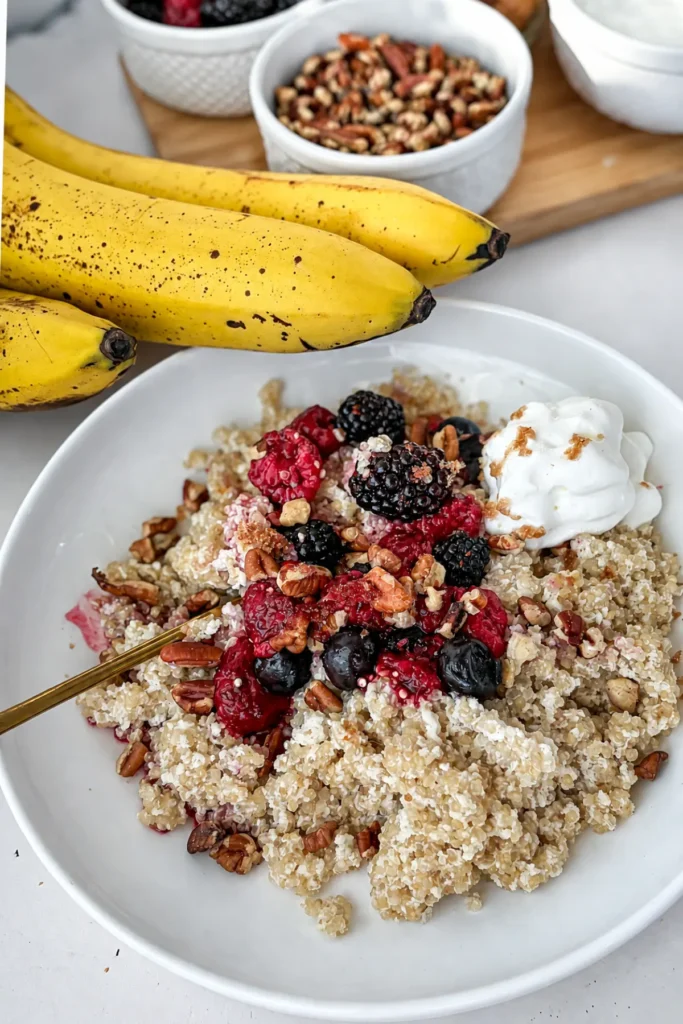 A close-up of a large bowl of coconut quinoa with protein powder topped with fresh berries and whipped cream.