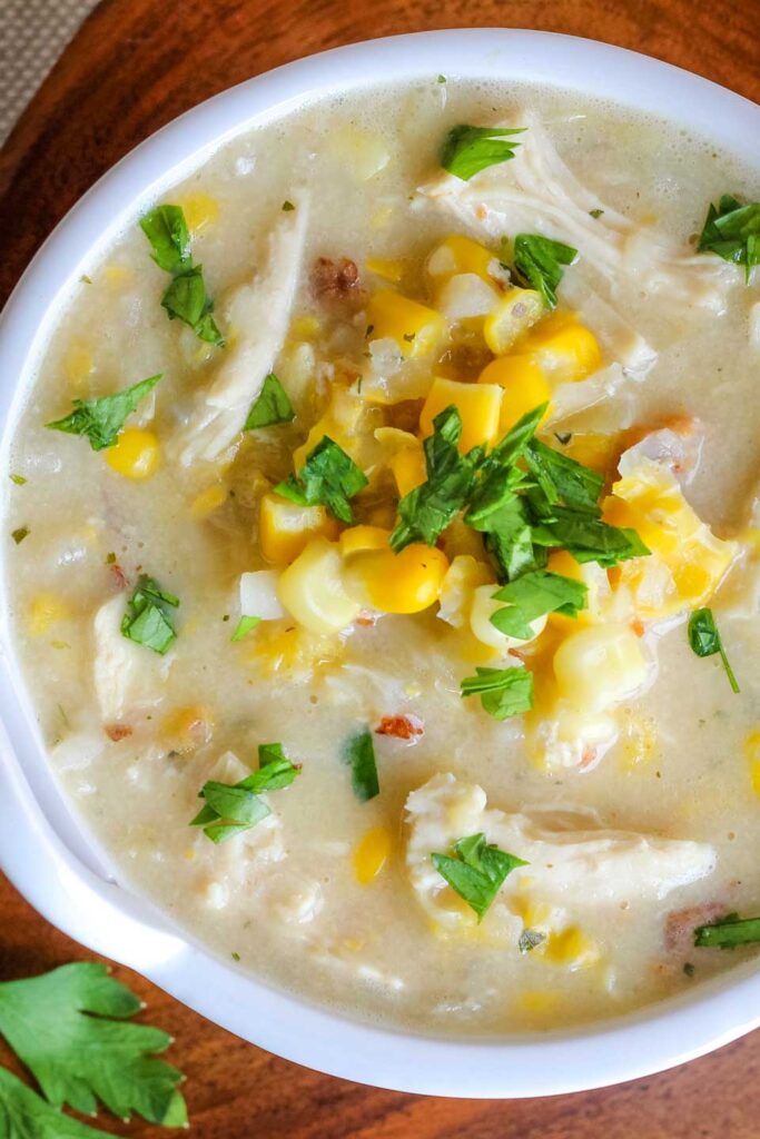 Crock-pot corn chowder with chicken in a bowl and topped with shredded cheese and green onions.