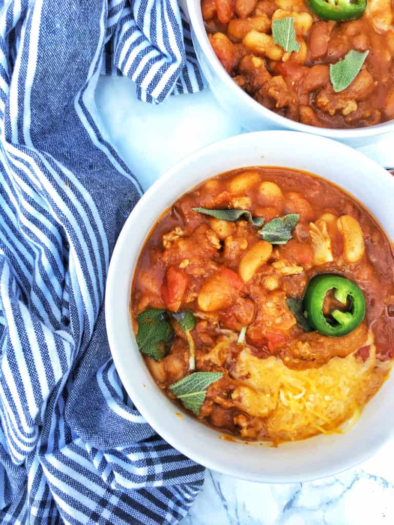 A birds-eye view of a slow cooker pumpkin chili in a bowl on a table next to a towel.