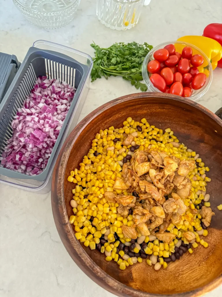 Adding the diced onions to a large bowl full of corn, beans and chicken on a counter.