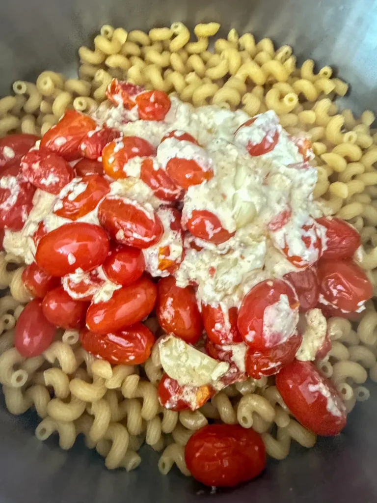 Adding the feta, tomato and garlic mixture to a pot of pasta.