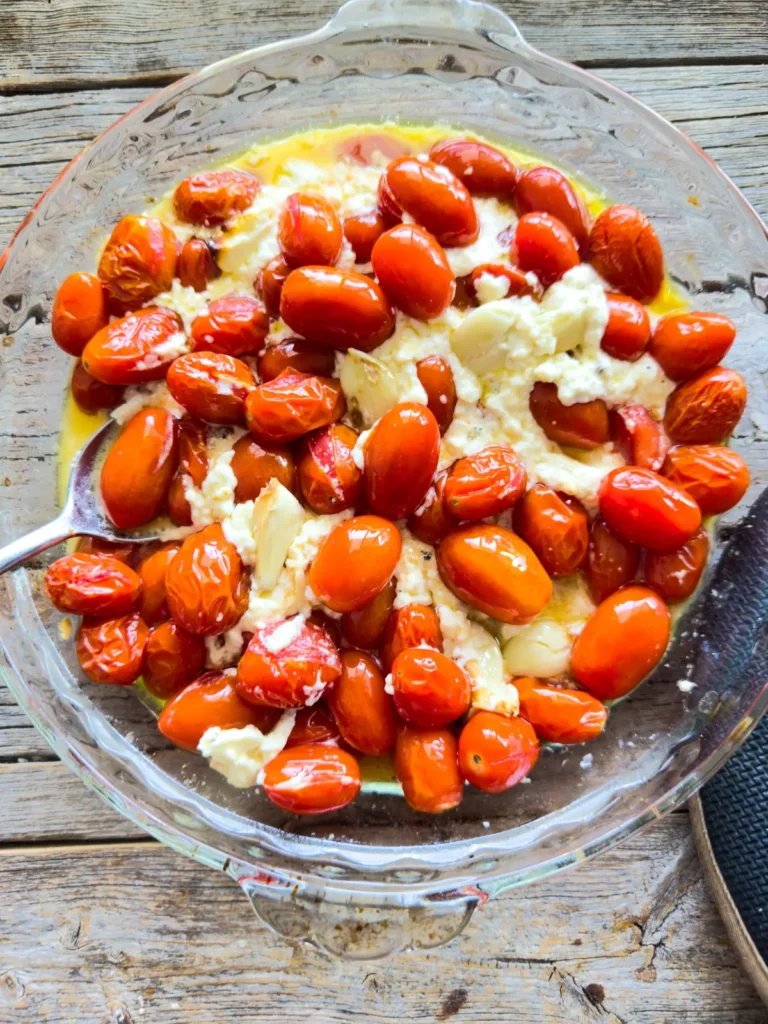 The baked feta, tomato and garlic mixture in a glass baking dish on a counter.