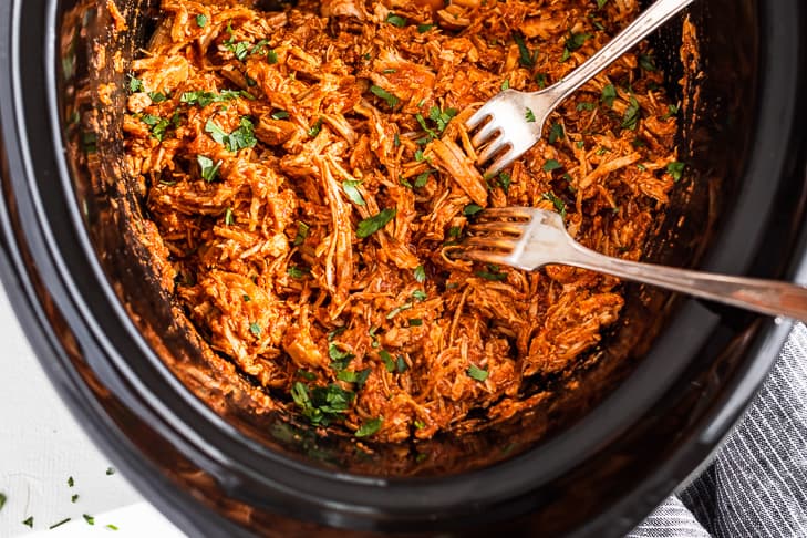 High protein slow cooker chipotle chicken in a slow cooker being shredded with two forks.