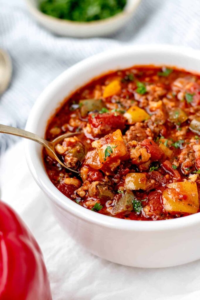 A bowl of unstuffed pepper soup on a table with a spoon in it.