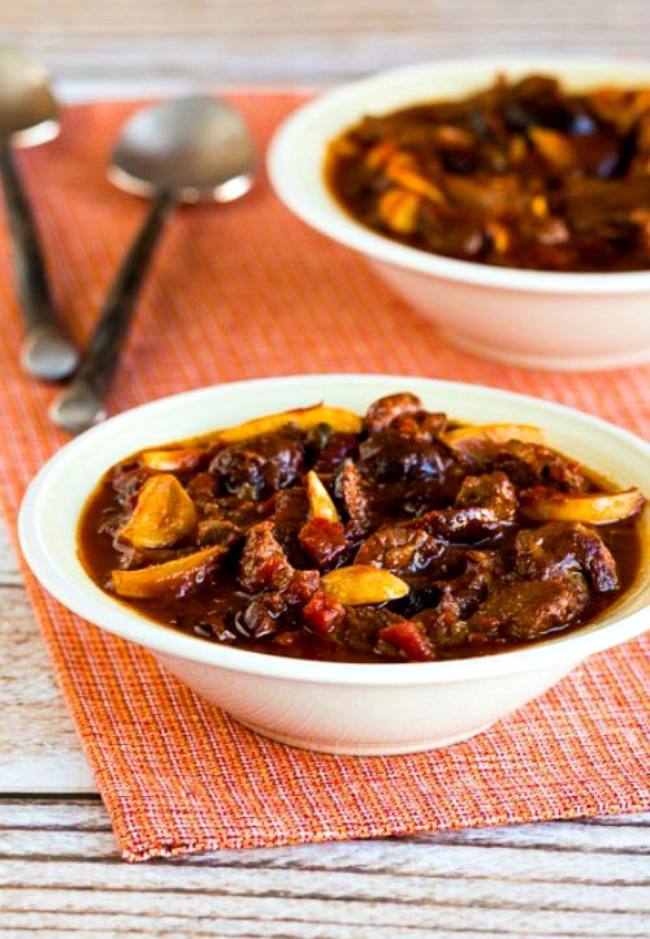 Two bowls of garlic beef stew on a placemat next to spoons.