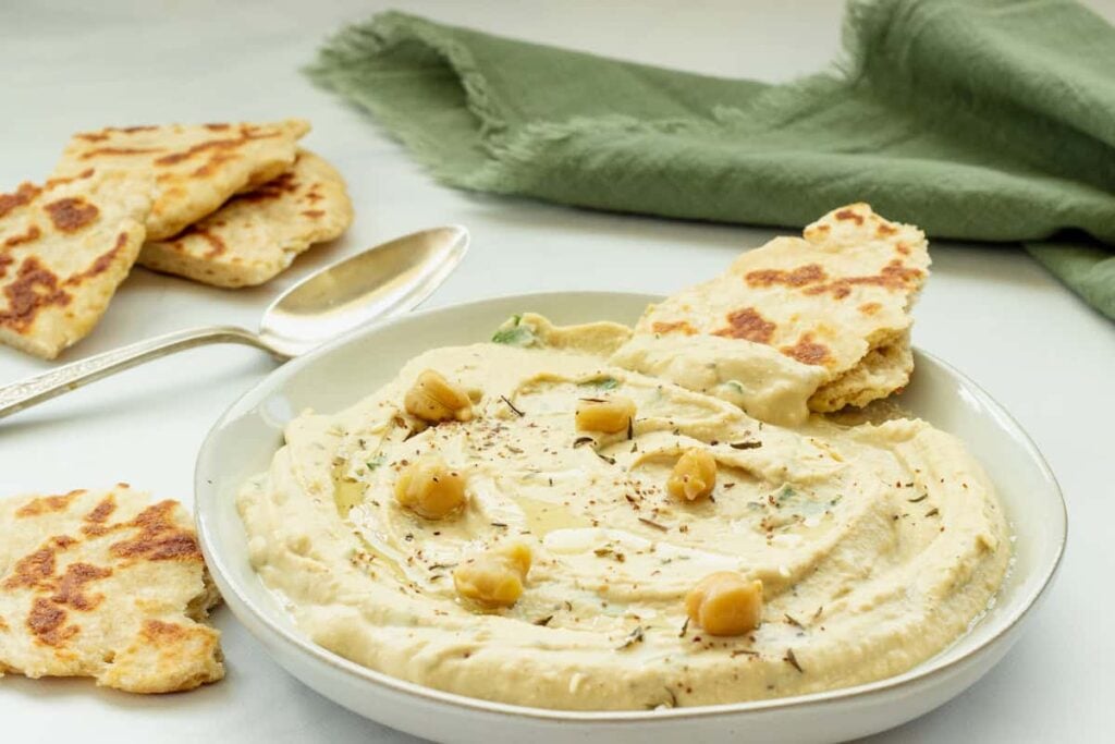 A big bowl of hummus next to pita dippers on a counter.