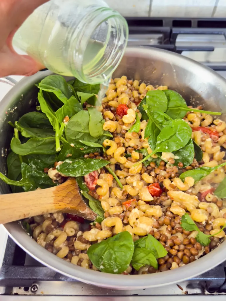 Pouring reserved pasta water into a pot with the feta tomato pasta in it.