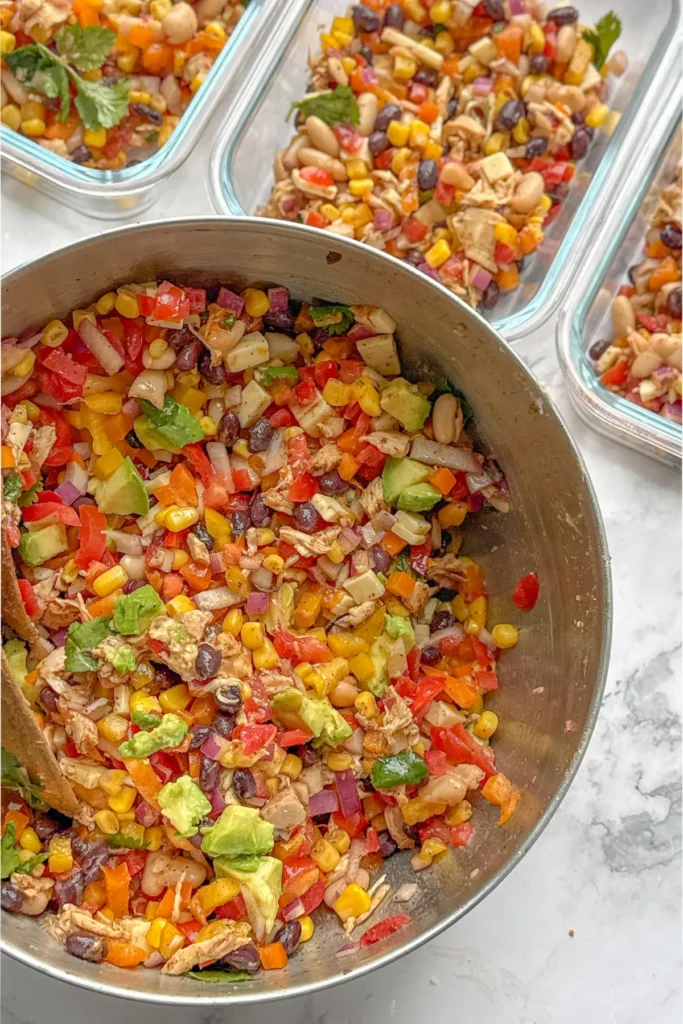 A birds-eye view of a big bowl of Mexican dense bean salad next to meal prep containers.