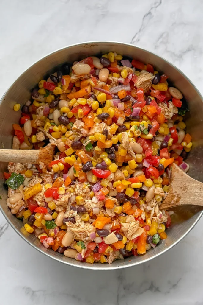 A birds-eye view of a big bowl of Mexican dense bean salad with two wooden spoons in it.
