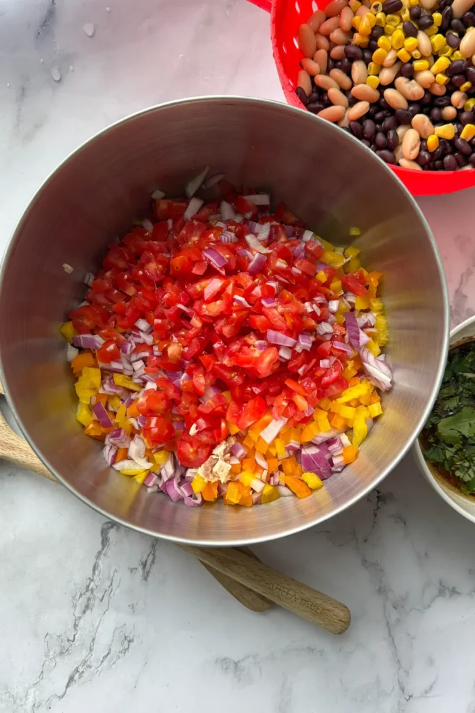 A large bowl of chopped vegetables and chicken with the corn and beans in a strainer on the side as well as the sauce on a counter.