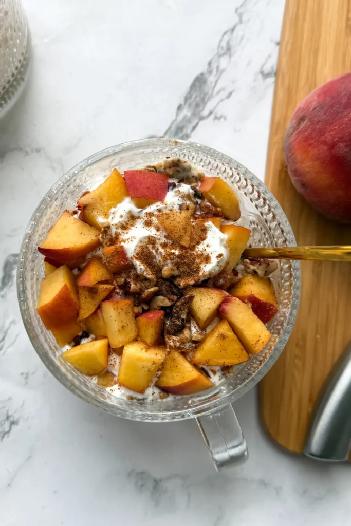 A birds-eye view of a bowl of peach cobbler overnight oats with a gold spoon digging into them on a counter.
