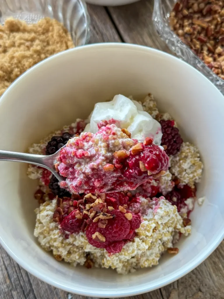 A spoonful of breakfast quinoa with coconut milk and berries over a bowl of quinoa.