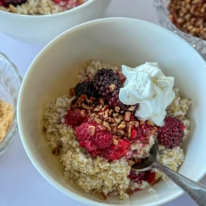 A close-up of a creamy coconut milk quinoa bowl topped with berries and nuts on a counter.