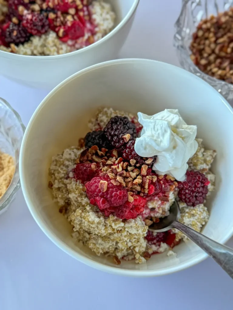 A close-up of a creamy coconut milk quinoa bowl topped with berries and nuts on a counter.