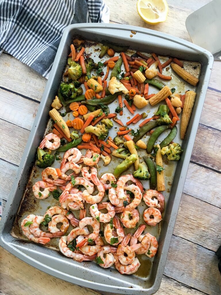 Baked shrimp and Asian vegetables on a sheet pan on a table.