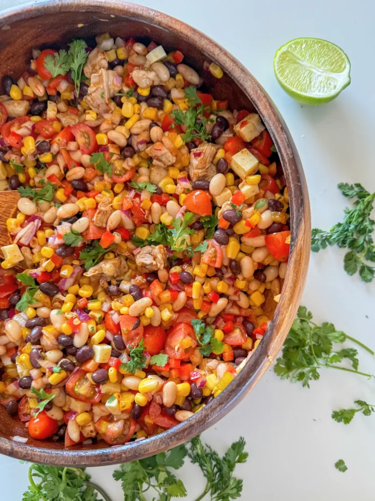 A birds-eye view of the taco style dense bean salad in a large wooden bowl on a counter.