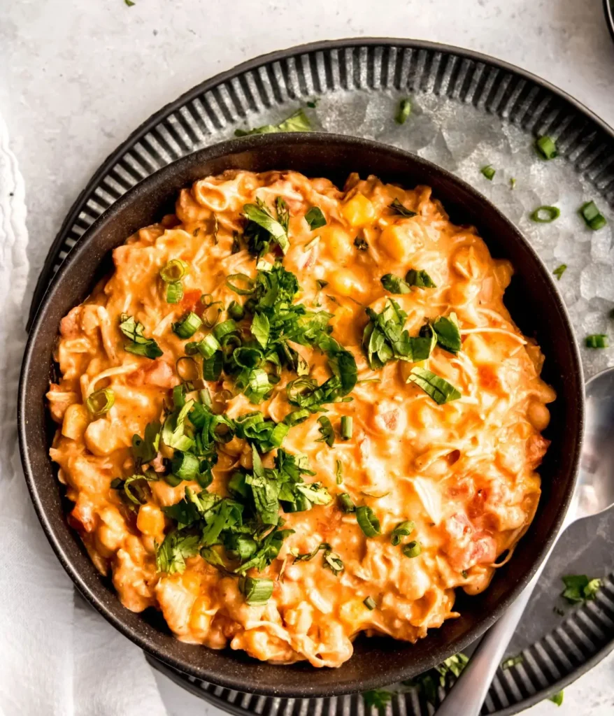 A large bowl of buffalo chicken chili on a platter next to a spoon on a table.