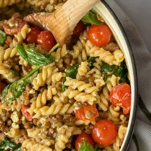 The right side, close-up of a large pot of high protein lentil pasta with garlic and tomatoes with a wooden spoon in it.