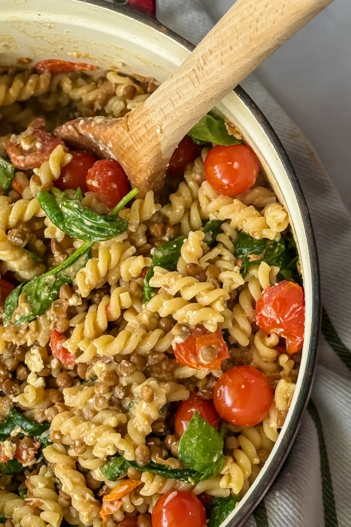 The right side, close-up of a large pot of high protein lentil pasta with garlic and tomatoes with a wooden spoon in it.