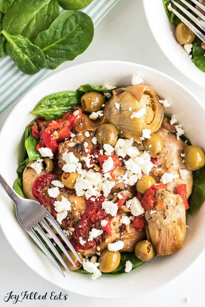 Crock pot Mediterranean chicken in a bowl topped with feta cheese and olives on a table.