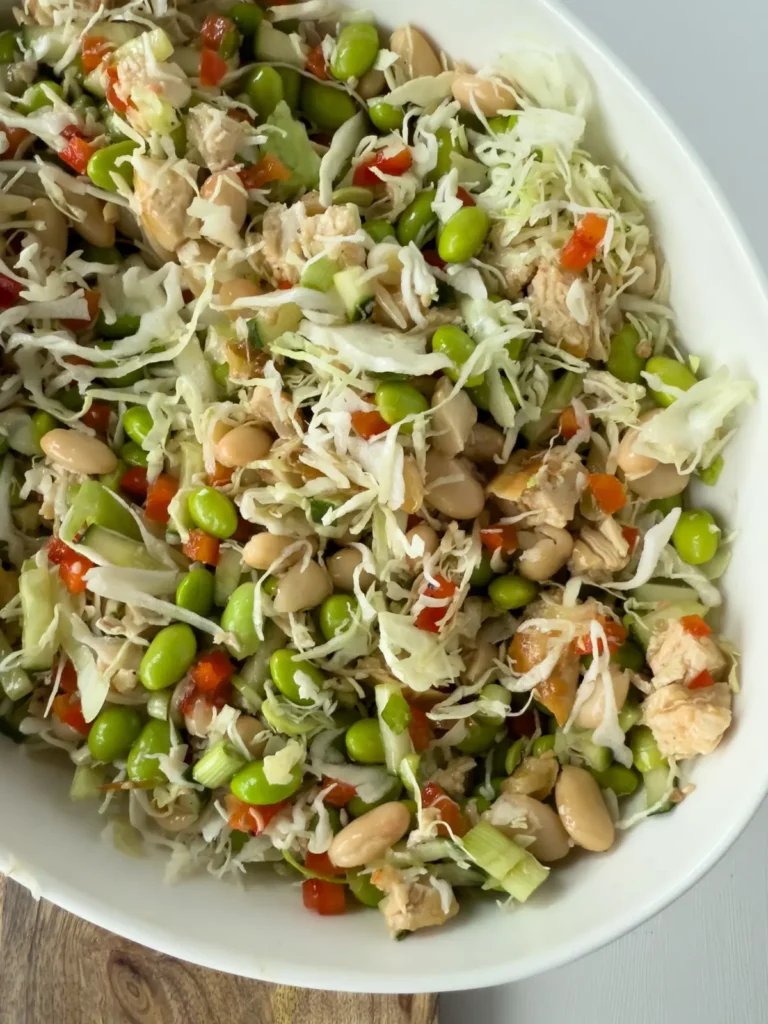 An Asian inspired dense bean salad with edamame beans in a large aluminum bowl on a counter next to an Italian dense bean salad.