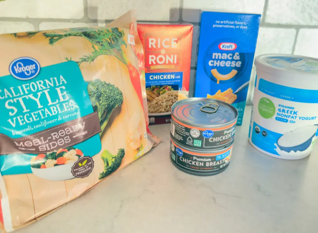 Budget friendly foods like frozen vegetables, Rice-A-Roni, canned chicken and Greek yogurt on a counter.