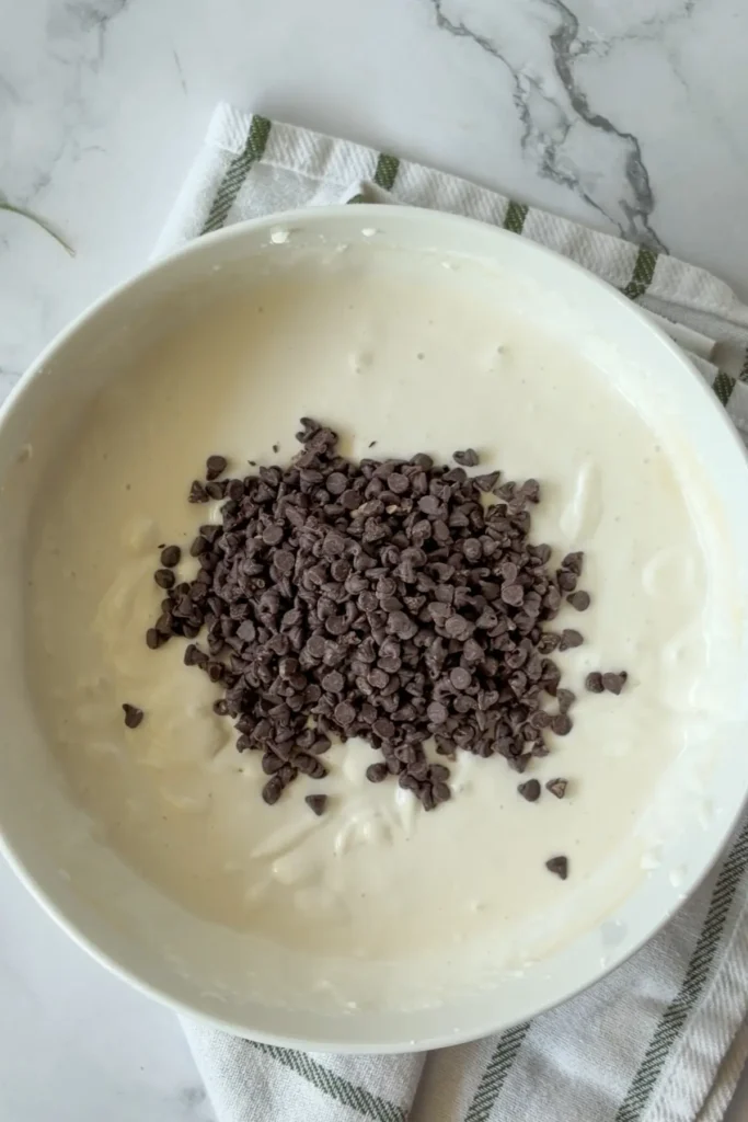 Adding mini chocolate chips to the bowl of s'mores dip.