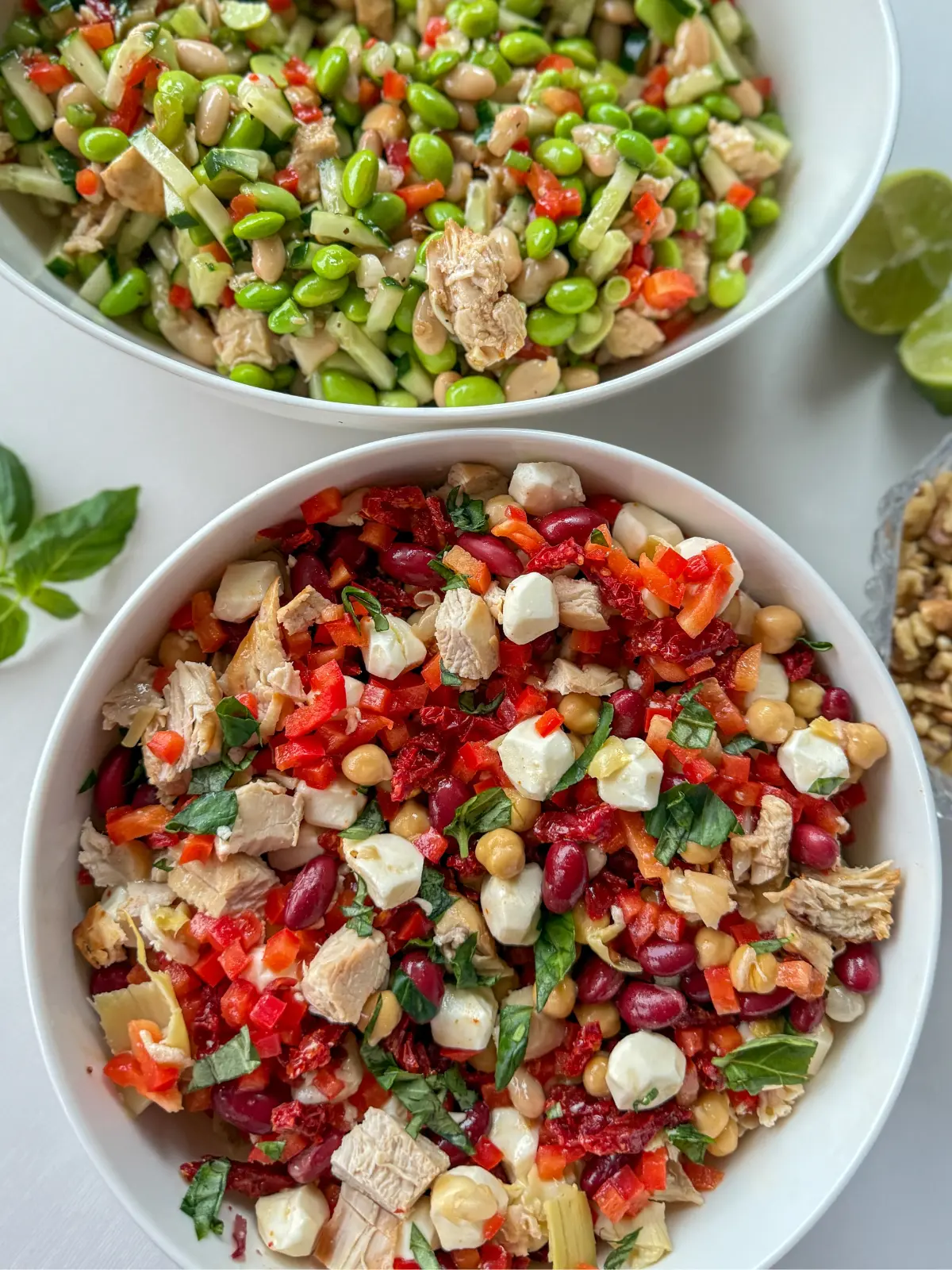 An Italian dense bean salad in a large white bowl next to an Asian-inspired dense bean salad in an oval white bowl on a counter.