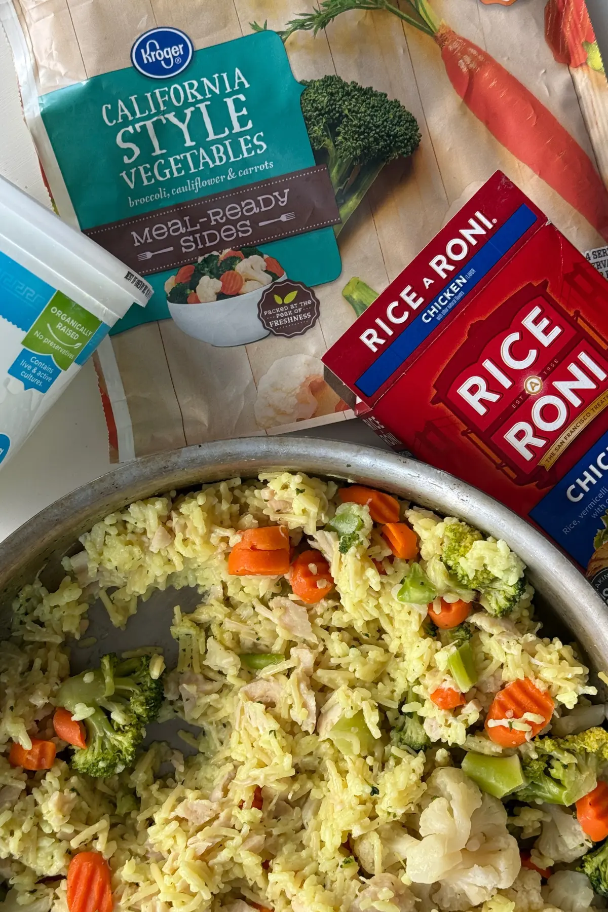 A large pan of healthier Rice-A-Roni on a counter next to an empty box of Rice-A-Roni and frozen vegetables.