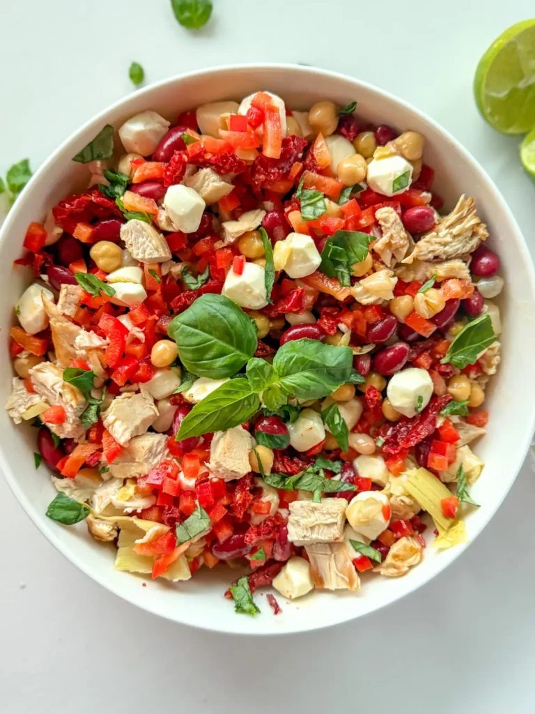 An Italian dense bean salad garnished with basil leaves in a large white bowl on a counter.