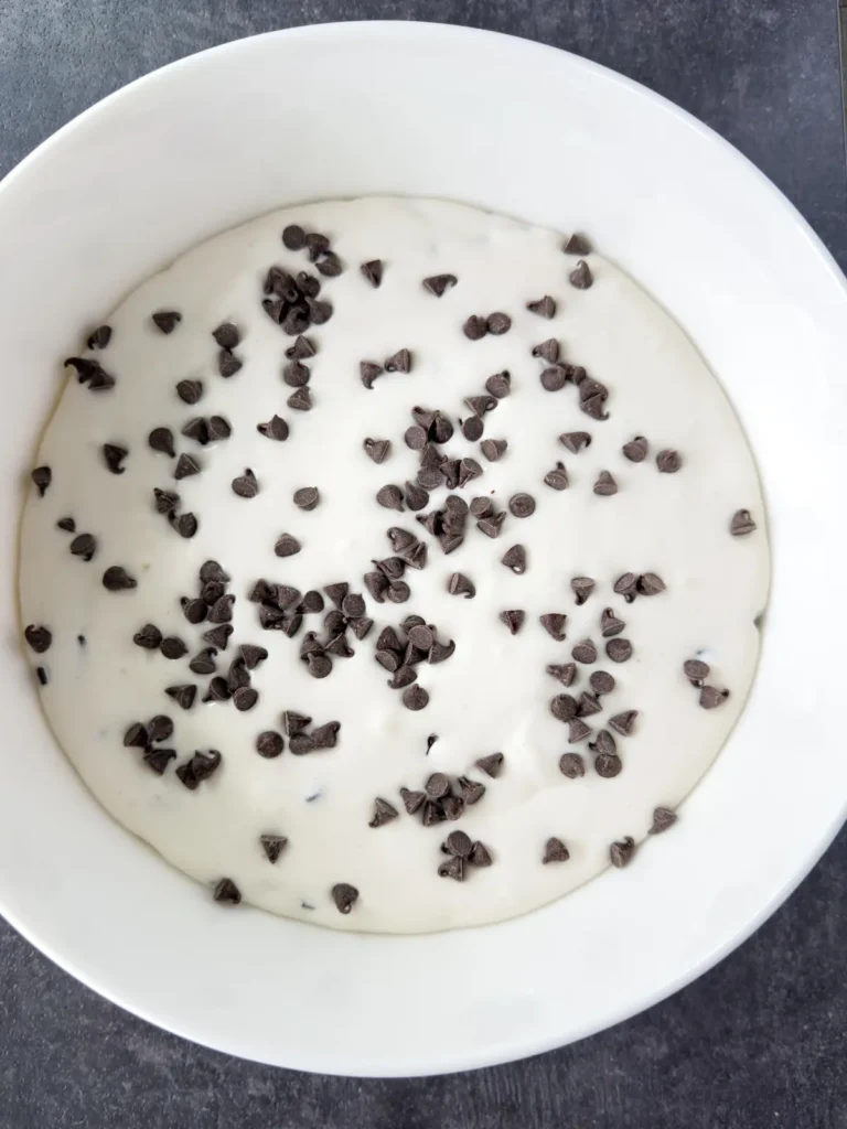 Adding mini chocolate chips to a bowl of the s'mores dip with cottage cheese.