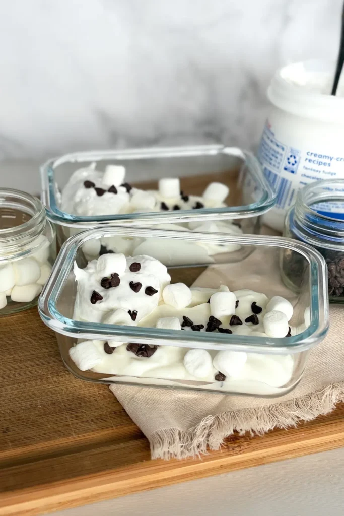 Two small snack storage containers with Greek yogurt pudding on a wood cutting board.