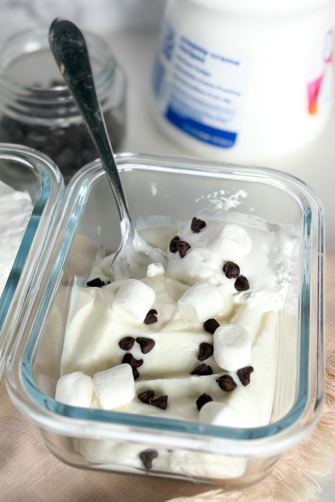 A spoon digging into the s'mores Greek yogurt next to a container of marshmallow fluff.
