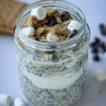 A fully loaded s'mores overnight oats topped with marshmallows, graham crackers and chocolate chips on a counter.