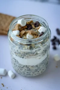 A fully loaded s'mores overnight oats topped with marshmallows, graham crackers and chocolate chips on a counter.